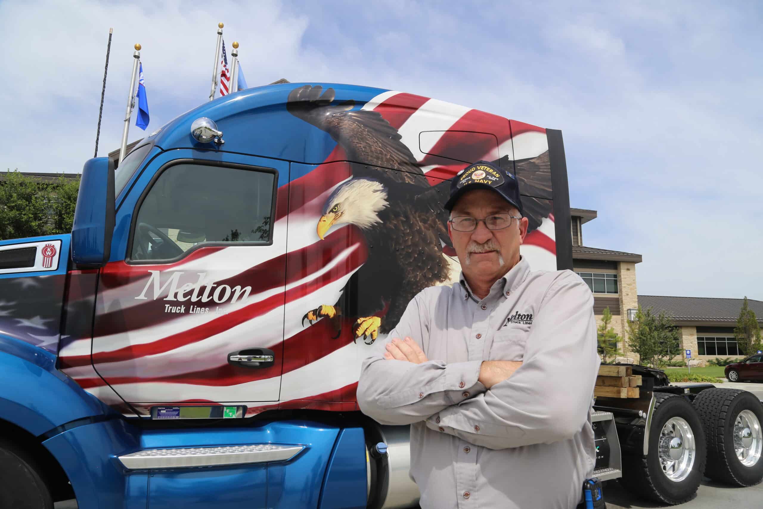 Military veteran flatbed driver standing in front of military wrapped flatbed truck