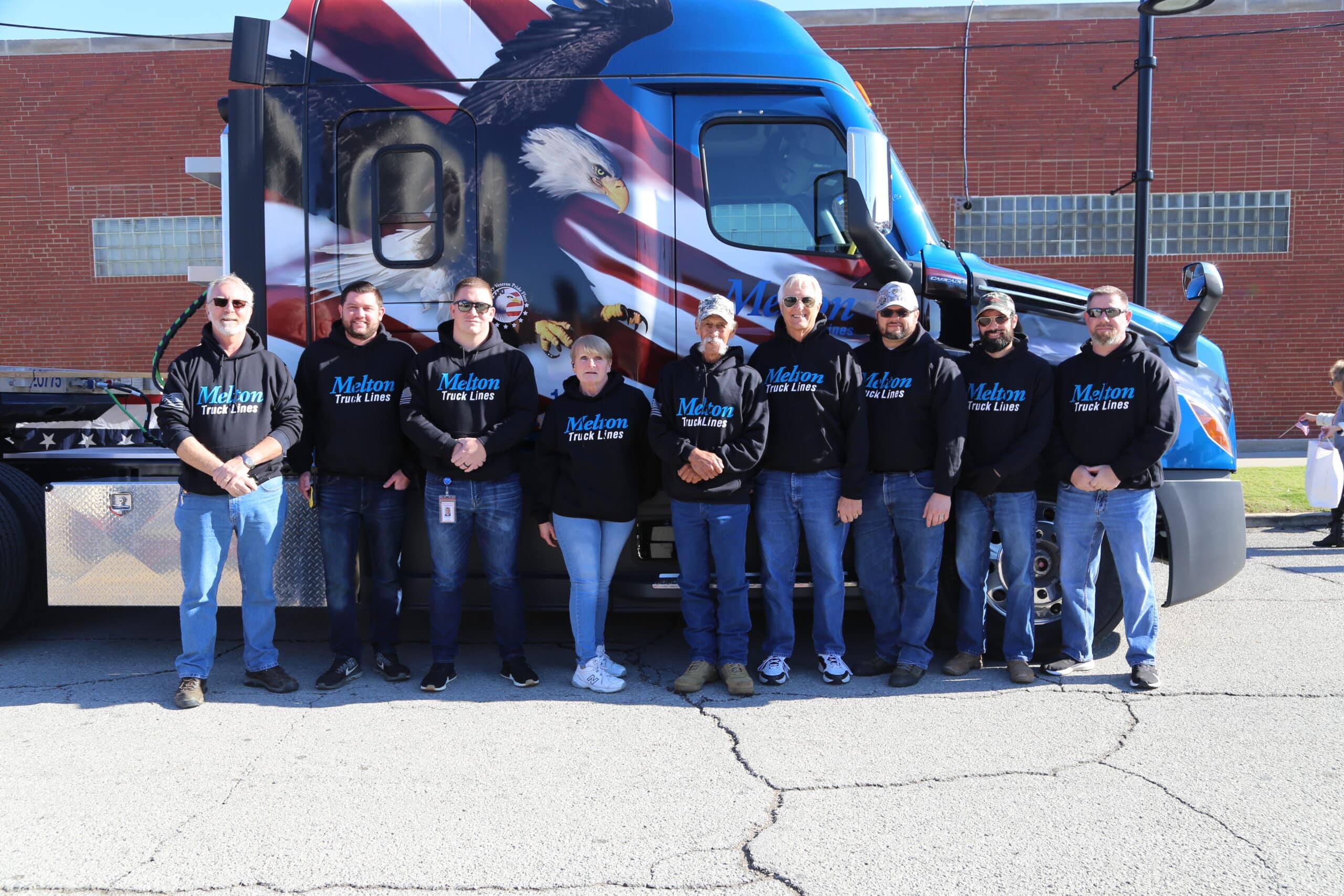Group of Melton's military veteran employees standing in front of military wrapped flatbed truck
