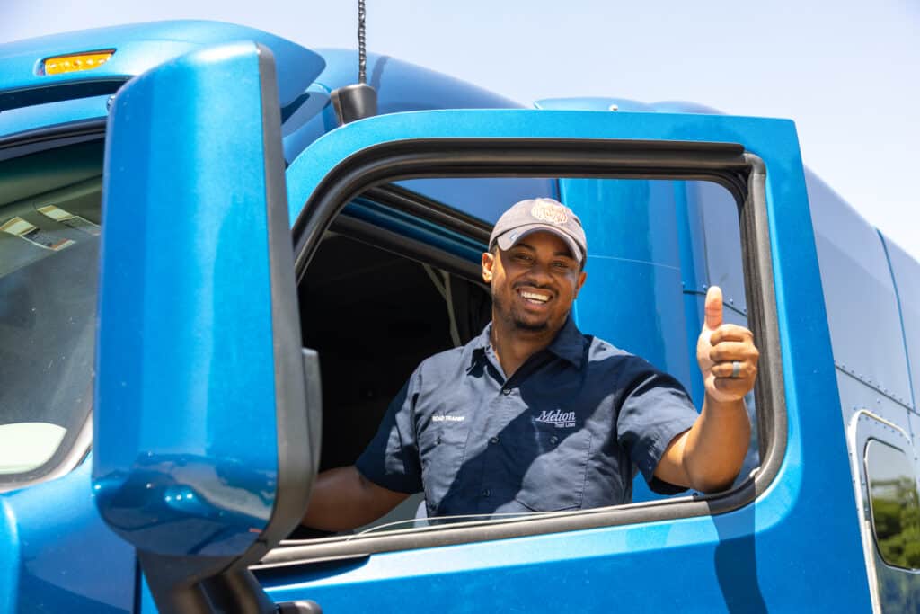 Flatbed driver sitting in flatbed truck giving thumbs up