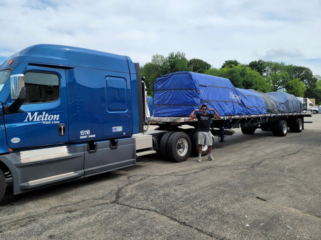 Melton flatbed driver posing in front of a tarped load on a melton flatbed truck