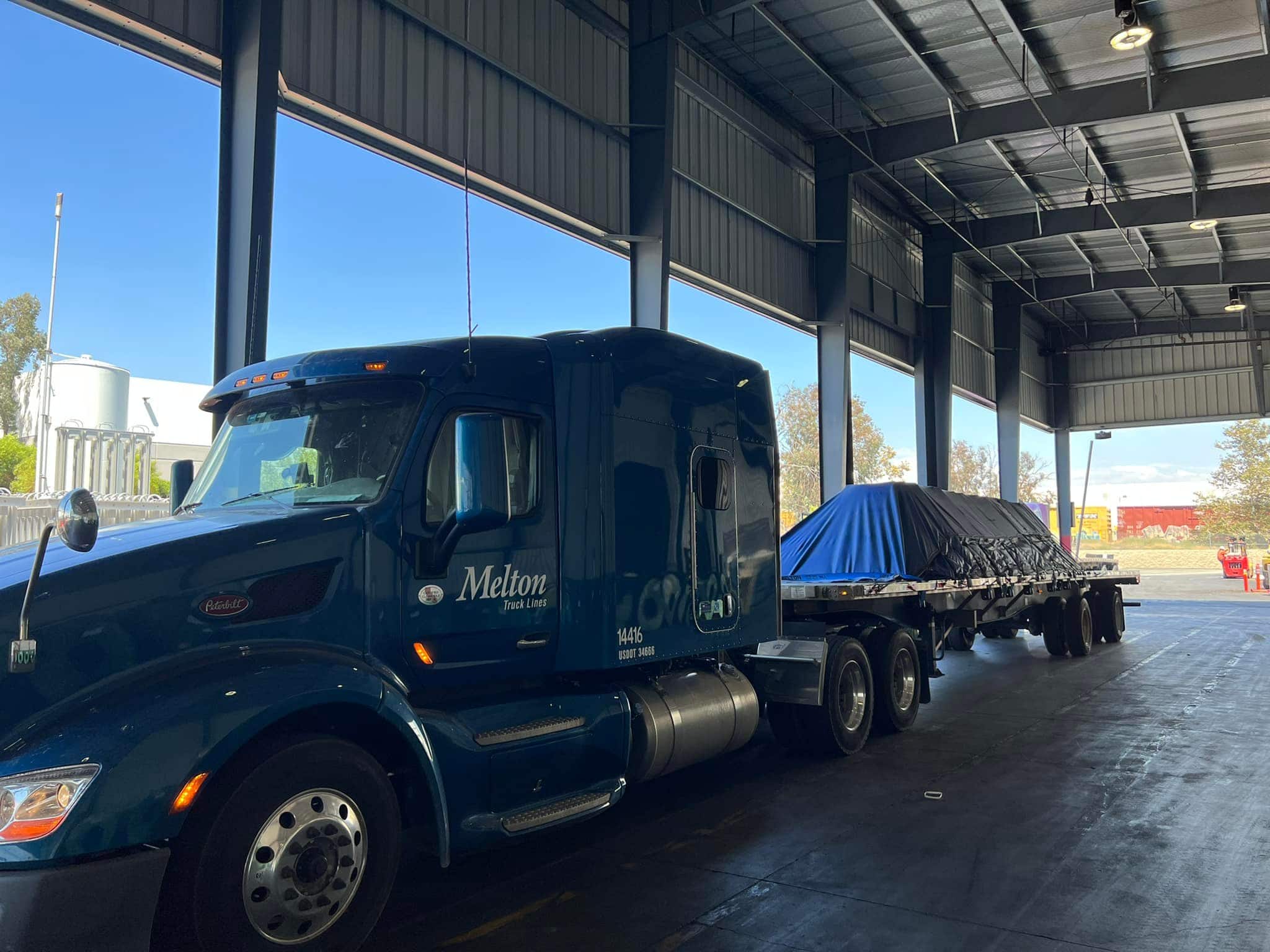 Melton flatbed truck with a tarped load on its trailer.