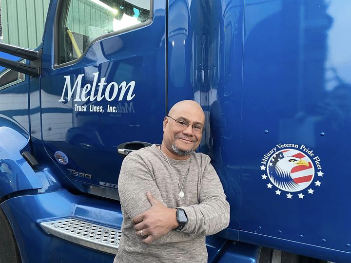 New veteran truck driver Jose G poses next to his veteran sticker on his truck