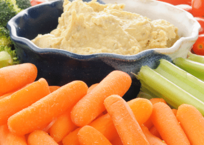 A bowl of hummus surrounded with sliced vegetables