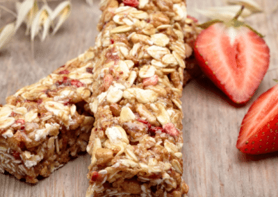 Two granola bars next to a sliced strawberry