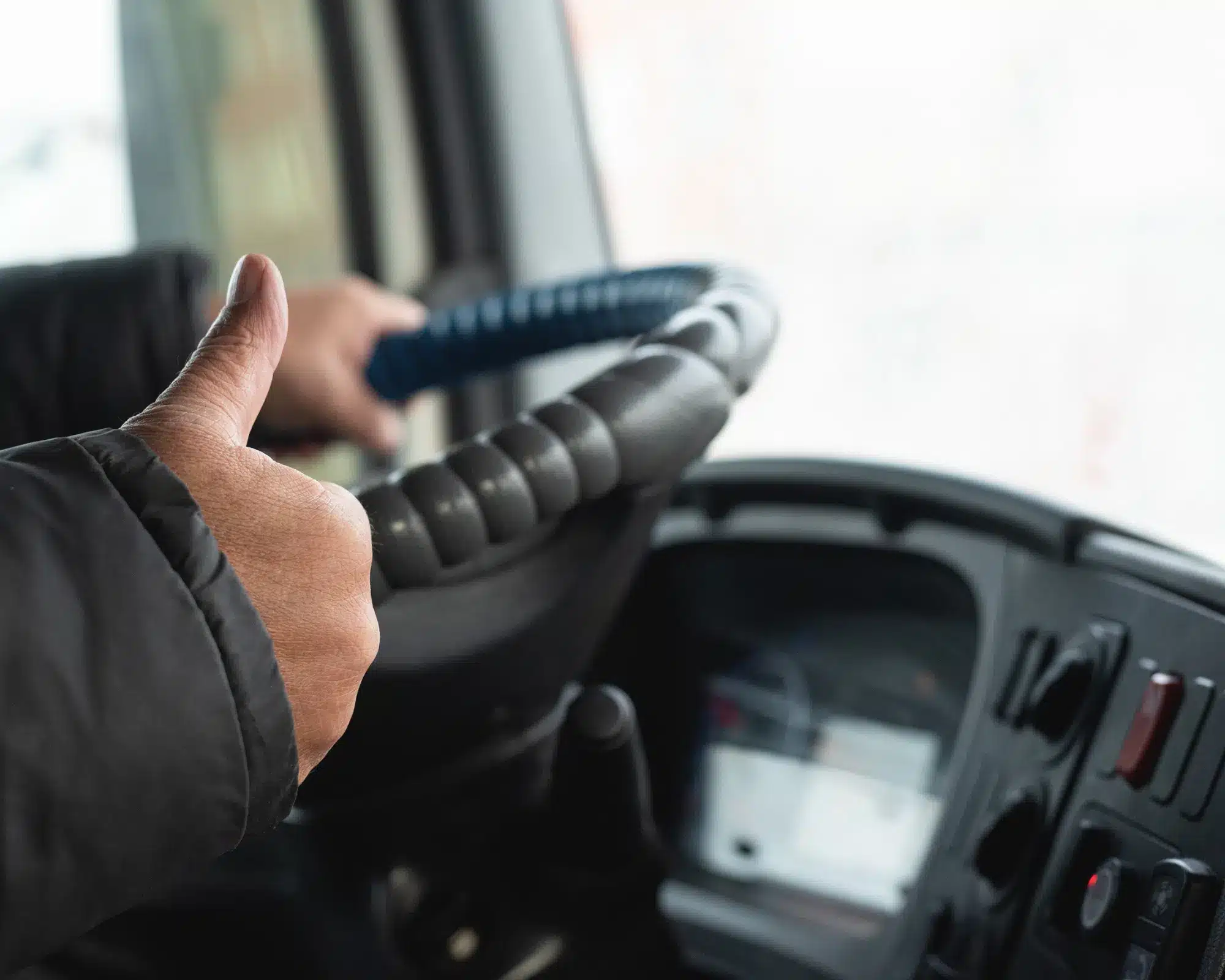 A hand on the steering wheel while the other does a thumbs up