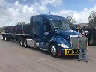 driver standing in front of a melton flatbed truck hauling an over dimensional load