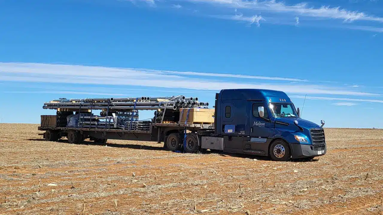 Melton truck with a load of pipes parked in an empty field.