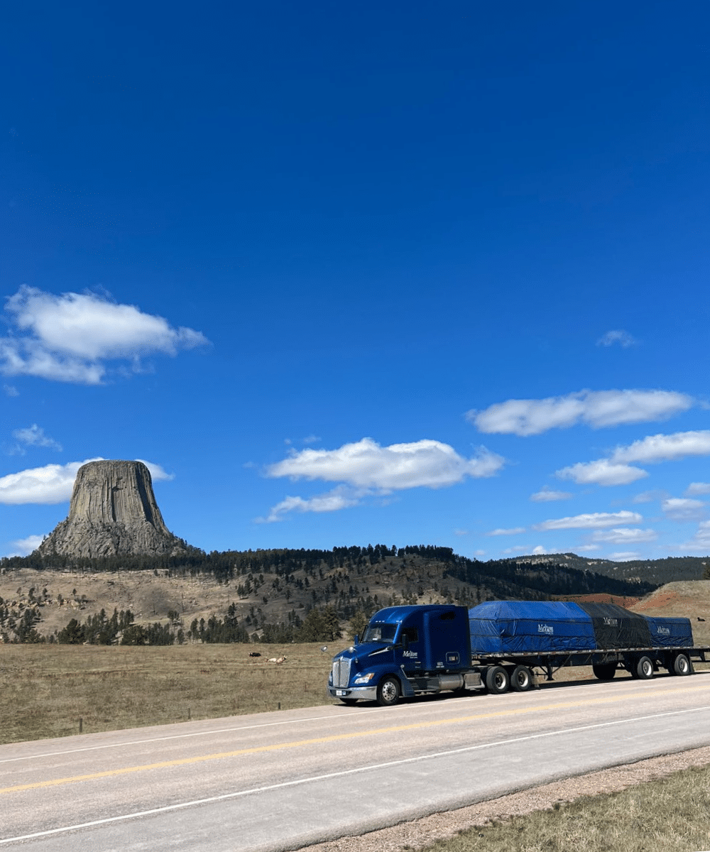 Melton truck driving down a road with a rock formation in the background