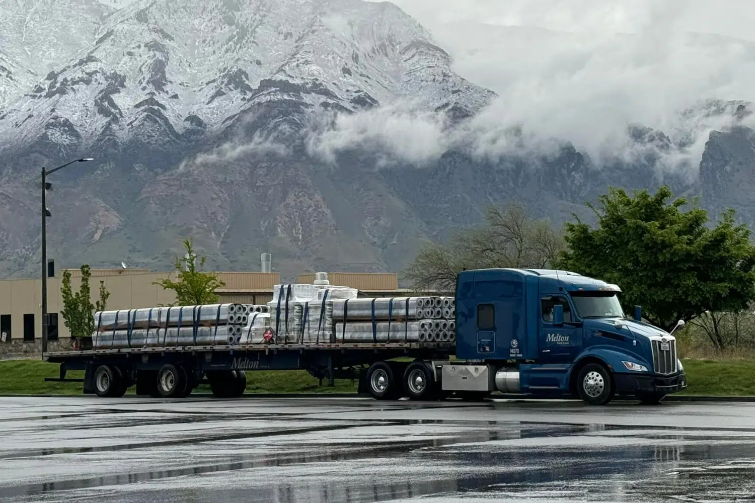 A Melton truck with a secured load parked in front of a mountain