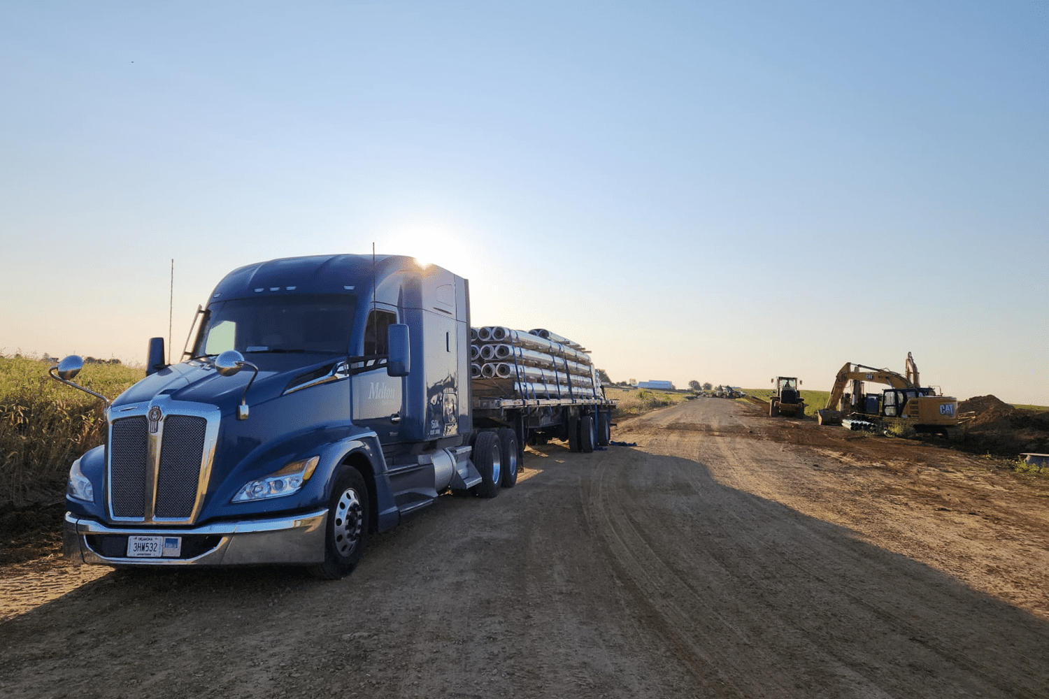 A Melton truck with a load of pipes parked on a dirt road