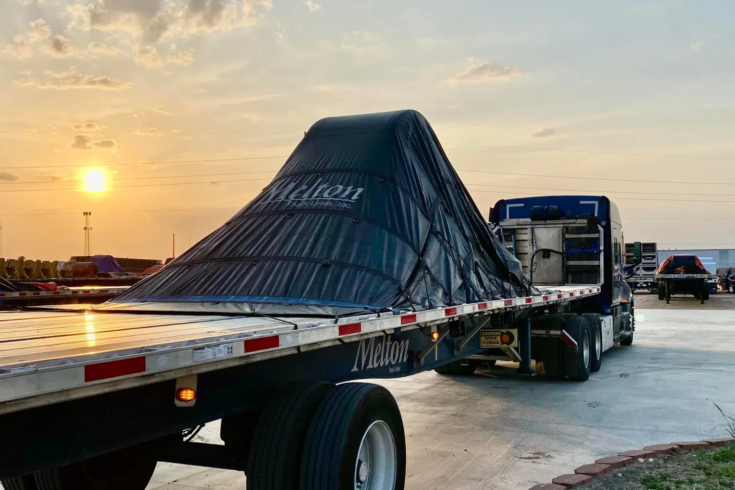 A Melton truck parked in the sunset with a tarp over a load