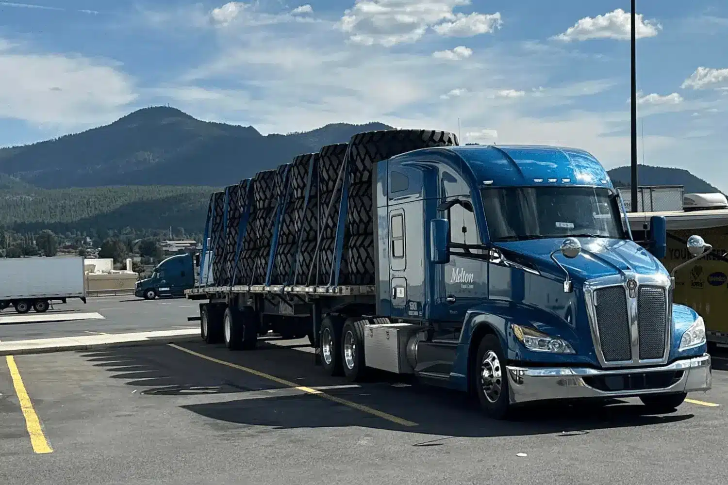 Melton flatbed truck with a load of tires parked in front of a mountain