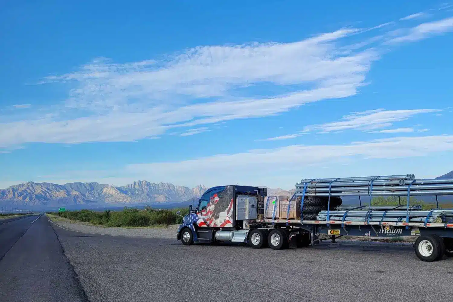 A Melton truck parked on the side of a highway with a mountain range in the background