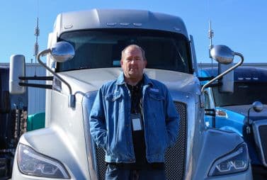 A Melton driver standing in front of his silver Ambassador flatbed truck.