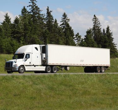 A white dry van truck driving down a highway with trees in the background