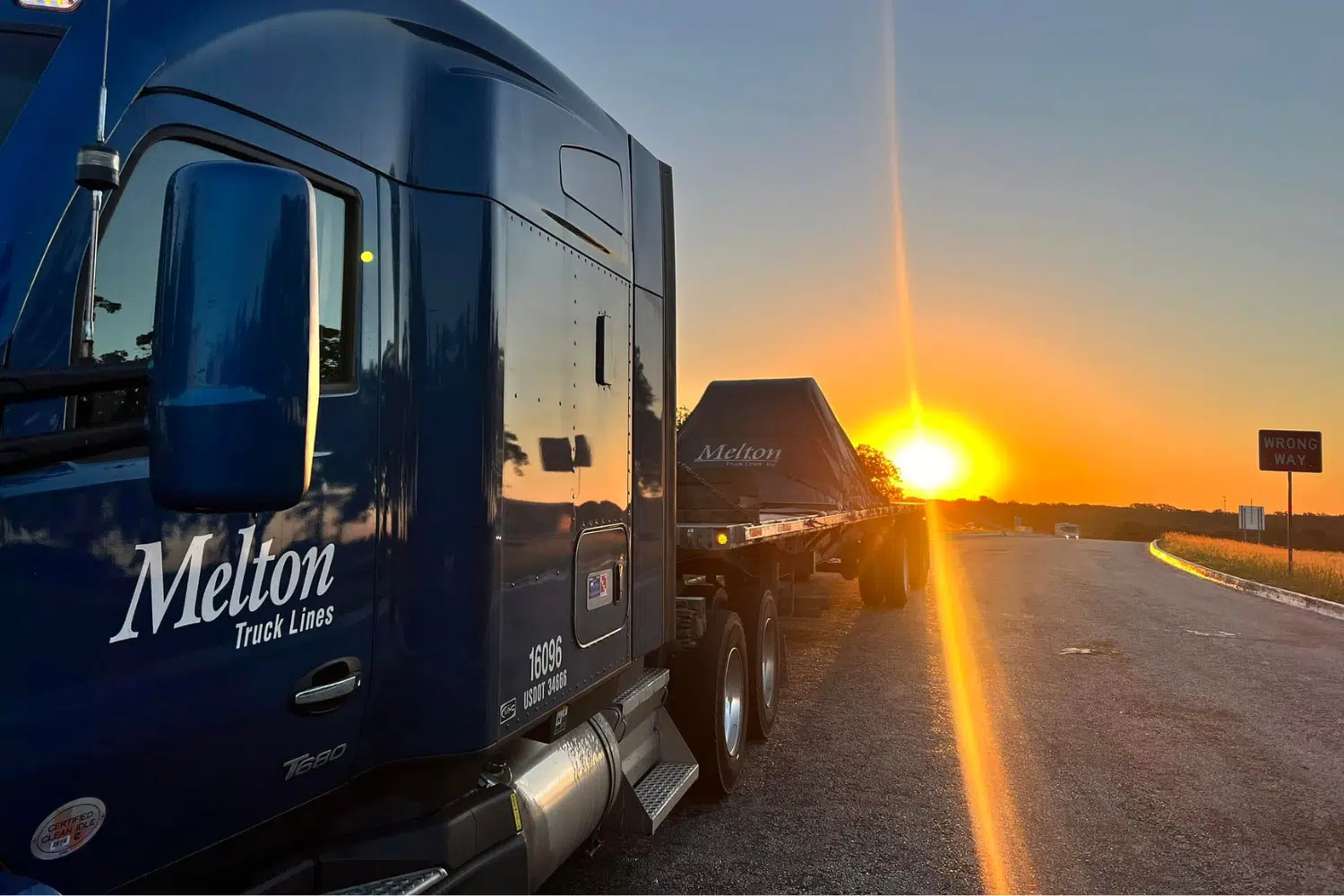 A Melton truck with a tarped load parked in front of a sunset.