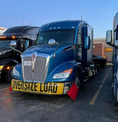 Melton truck with red flags and an over-dimensional load banner parked in a lot.