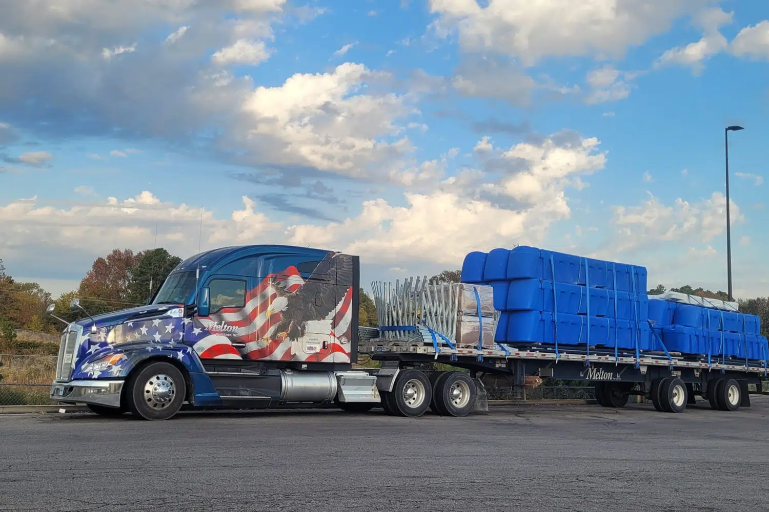 A Melton truck with a patriotic wrap hauling a tarped load.