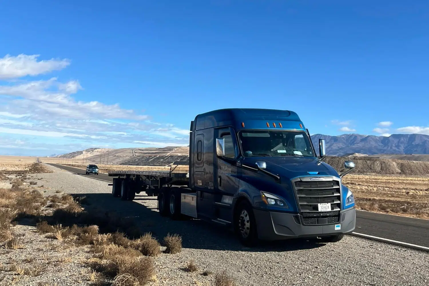 A Melton truck with an empty flatbed trailer parked on the side of a desert road.