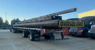 A Melton truck loaded with steel beams. A yellow Oversize Load flag is attached to the back.