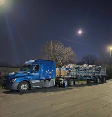 A blue Melton truck with a loaded flatbed trailer