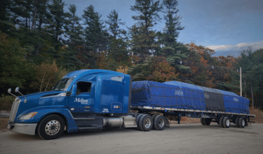 Melton truck with a tarp parked by some trees