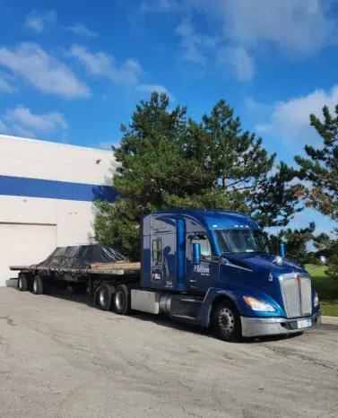 A Melton truck parked in front of a building with a tarped flatbed load