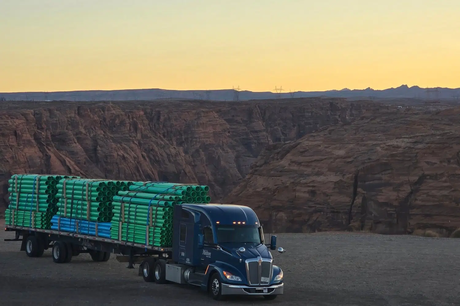 Melton truck parked by a cliff with a secured load of pipes