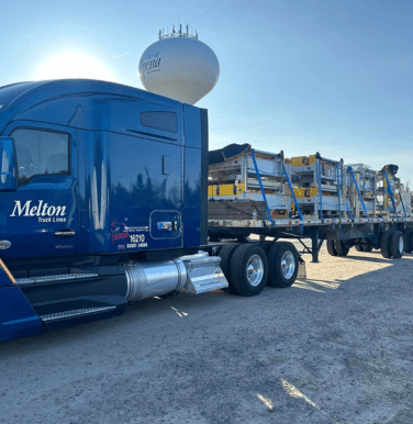 A Melton truck with a secured load in front of a water tower