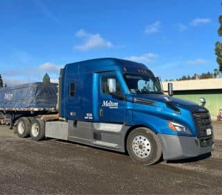 A Melton truck parked in front of a building with a tarped load