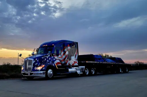 A Melton truck with a patriotic wrap and a tarped load in the sunset