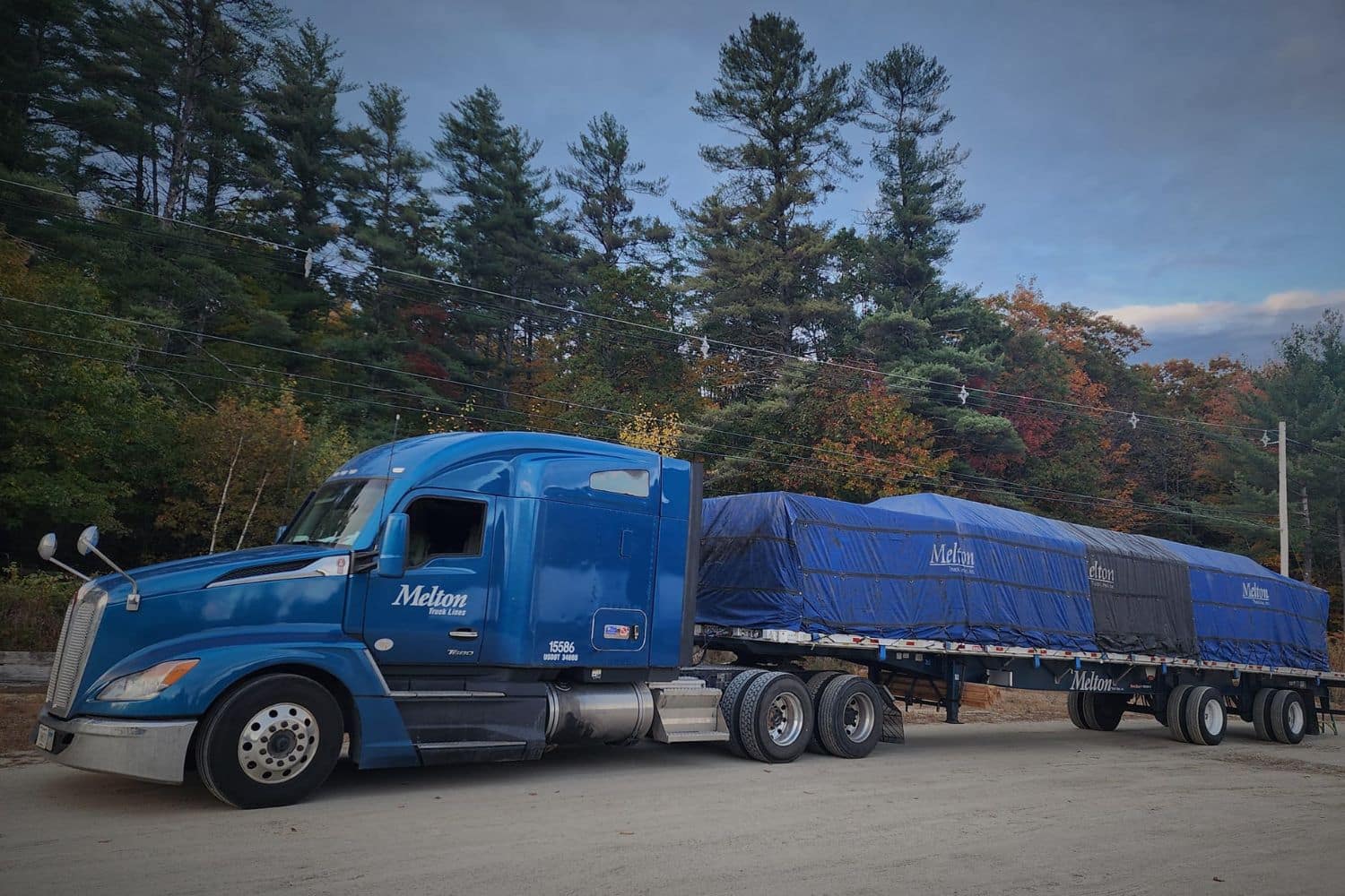 A Melton truck with a tarped load parked by trees