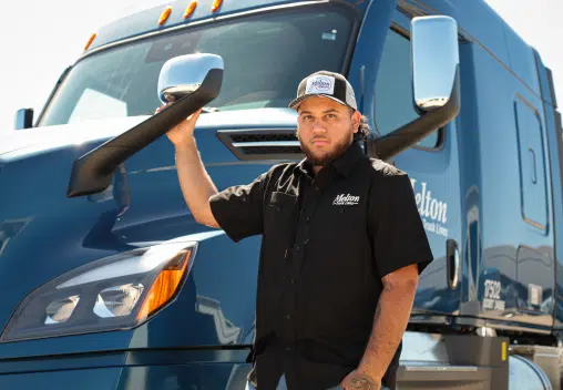 A man standing in front of a Melton truck holding onto the rearview mirror