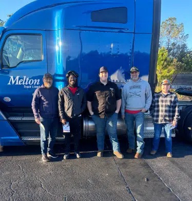 CDL school students posing in front of a blue semi truck