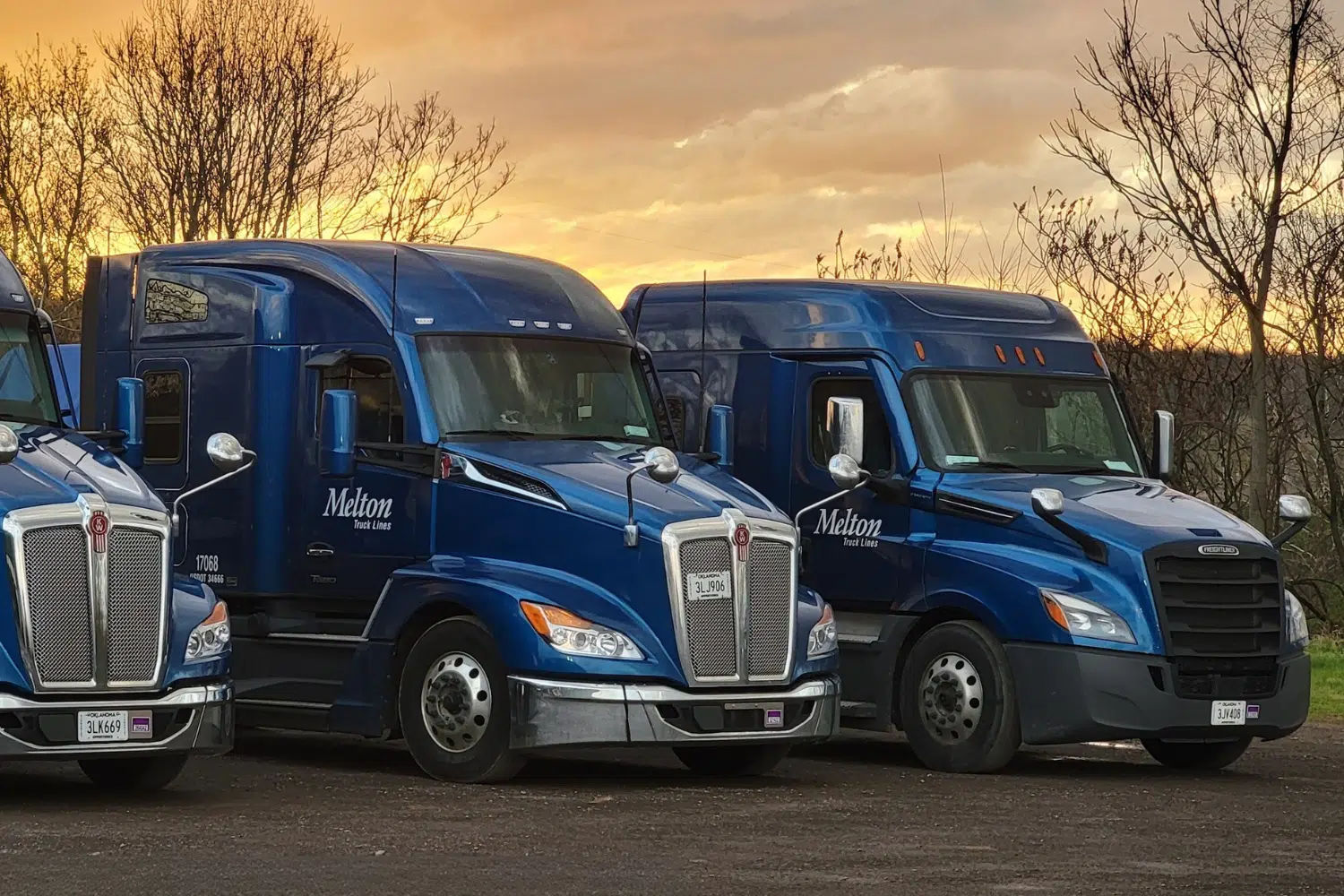 Melton flatbed trucks parked next to each other with a yellow sunset in the background